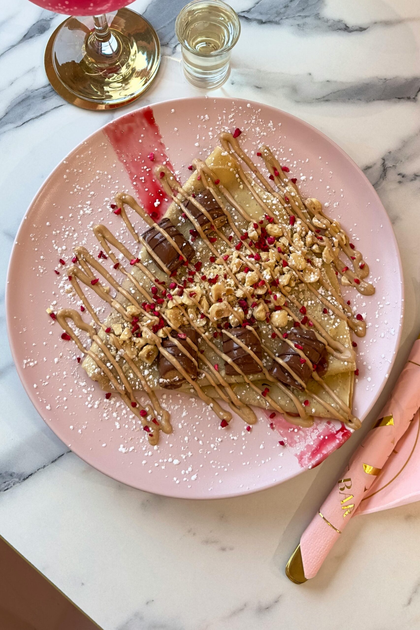 Stylish marble table with cocktails, dessert crepes and floral decor in a chic cafe.